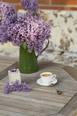 Green vase with Lilac flower, candle light and caup of porcelain coffee  on wooden table at the outoor garden