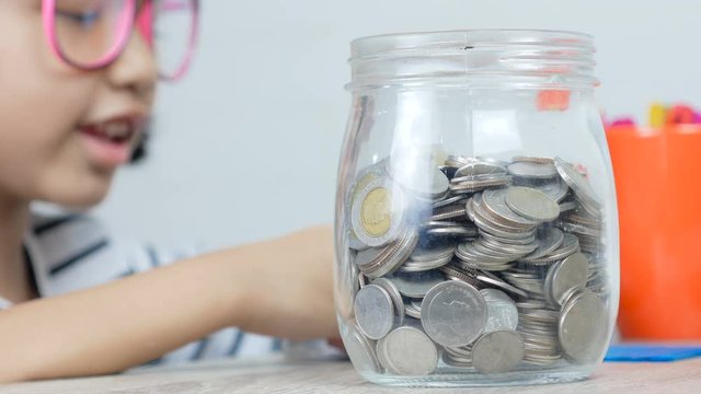 Asian little girl putting the coin in to a glass jar shallow depth of field select focus on jar