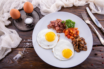 A breakfast from fried eggs with bacon and tomatoes, champignons and greens
