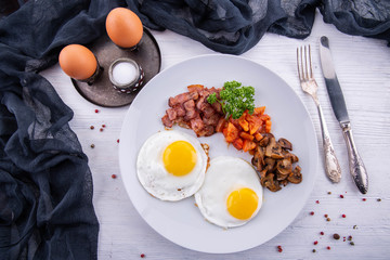 Fried eggs from two eggs which are pan fried are served with vegetables and fried bacon with greens
