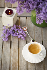 Green vase with Lilac flower, candle light and cup of porcelain coffee  on wooden table at the outdoor garden
