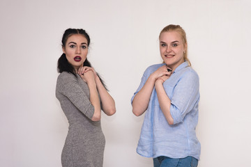 Portraits on the gray background of two girls girlfriends showing emotions.