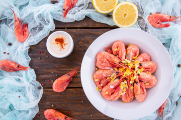 Shrimps boiled with sauce and pieces of a lemon on a dark wooden background