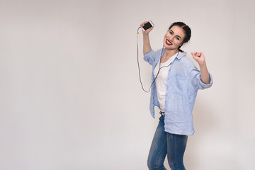 Portrait of a beautiful brunette girl in a shirt on a gray background with a smartphone.