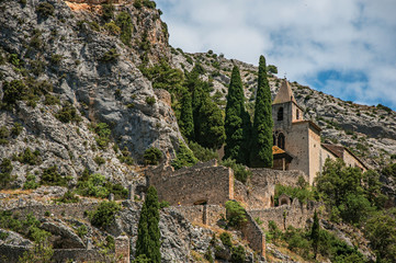 Fototapeta na wymiar View of the Notre-Dame de Beauvoir church amidst cliffs and rock stairway, above the graceful Moustiers-Sainte-Marie village. Alpes-de-Haute-Provence department, Provence region, southeastern France