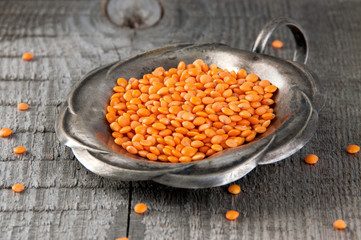 Red lentils in vintage silver jar on old wooden background.