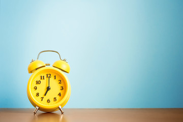 yellow alarm clock seven o'clock in the morning on the table against the blue wall. time for people...