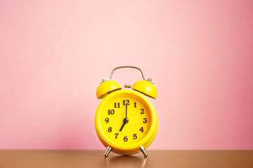 yellow alarm clock seven o'clock in the morning on the table against the pink wall. time for people to get to work, for kids to school
