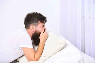 Fototapeta premium Man in shirt laying on bed, white wall on background. Nap and siesta concept. Macho with beard and mustache yawning, relaxing, having nap, rest. Guy on sleepy tired face yawning.