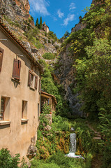 Fototapeta na wymiar View of houses near creek and bluff with church on top of cliff in the charming village of Moustiers-Sainte-Marie. In the Alpes-de-Haute-Provence department, Provence region, southeastern France