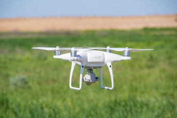The modern drone, quadrocopter is in the air against the background of the sky and grass