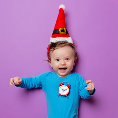 Little infant baby in Christmas hat with alarm clock on purple background