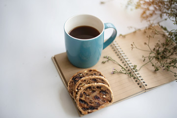 The blue ceramic coffee cup with black coffee put beside book and mixed fruit bread,on white desk