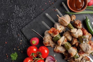 Seductive shish kebabs on skewers. Still life on a black background. Appetizing meat with fresh vegetables and sauce.