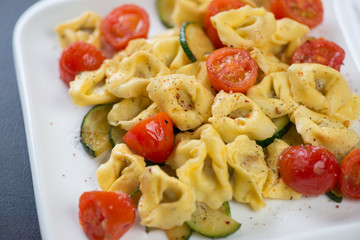 Close-up of tortellini with roasted cherry tomatoes and zucchini slices, selective focus