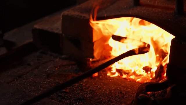 Closeup of a blacksmith fanning the flames of the furnace, using the tools prevents embers, sparks flying to the side in slow motion. Close-up of blacksmith's hand.
