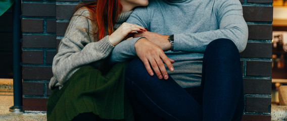 Fototapeta na wymiar the couple is sitting on the floor in an embrace. embrace. a female hand with a ring, a man's hand with a watch. talking. gray sweaters.