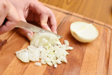 Fototapeta na wymiar Female hands using a knife cut a fresh onion on a cutting board. Close-up