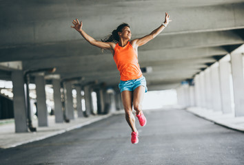 Young female runner jumps on the street,expressing positive emotion.She made her goal of the...