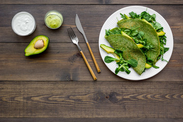 Obraz na płótnie Canvas Healthy vegetable pancake. Spinach pancakes served with cucumber, avocado and greenery on dark wooden background top view copy space