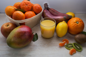 Fresh healthy tropical fruits. Summer food, vitamins concept.Basket of ripe mandarins,apple,mango,red bananas,lemons,orange and kiwi with glass of juicy.