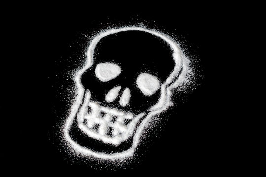 White sugar in shape of the skull isolated on black background. caution sign. deadly addiction