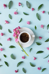Fototapeta na wymiar White cup with coffee on a blue background. Pattern of pink flowers and green leaves. Creative design. Concept. Flat lay