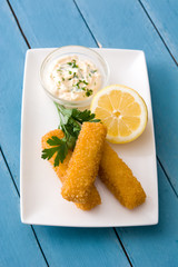 crispy fried fish fingers with lemon and sauce on blue wooden background. Top view