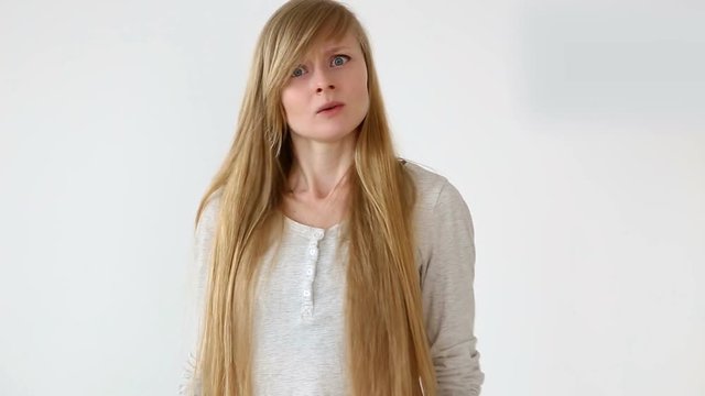 beautiful long-haired girl of European appearance with blond hair posing against white wall. emotions - denial and anger, disagree