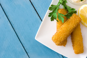 crispy fried fish fingers with lemon and sauce on blue wooden background. Top view. Copyspace