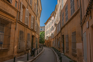 Fototapeta na wymiar Narrow alley with tall buildings in the shadow in Aix-en-Provence, a pleasant and lively town in the French countryside. Located in Bouches-du-Rhone department, Provence region, southeastern France