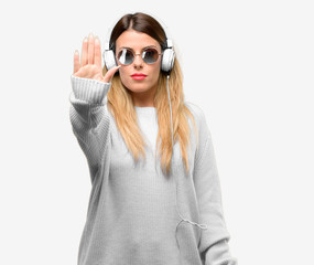 Young woman listen to music with headphone annoyed with bad attitude making stop sign with hand, saying no, expressing security, defense or restriction, maybe pushing