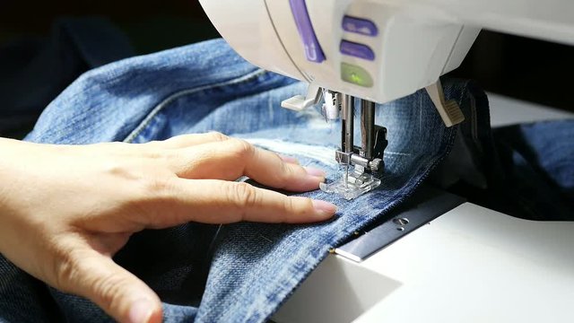 Woman doing jeans patchwork using sewing machine - home DIY sewing 