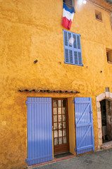 View of yellow house with blue blinds and flag, in the quiet and graceful village of Sillans-la-Cascade, on the way to Draguignan. Located in the Provence region, Var department, southeastern France