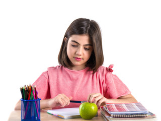 A beautiful school girl sits at the desk with apple and thinking. White background