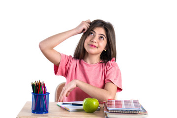 A beautiful school girl sits at the desk with apple and thinking. White background