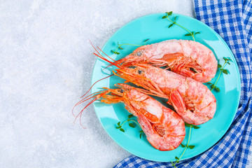Large royal raw frozen prawns on a blue plate with thyme and basil on a concrete table. Red shrimps. Top view.