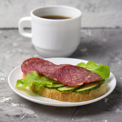cup of black coffee and sandwich with sausage, cucumber and salad square image