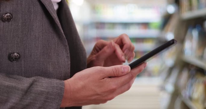 Shot of Caucasian woman's hands while she looks through photos on phone in store