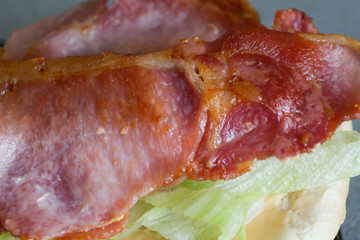 A close up of crispy bacon sitting on a bed of lettuce on top of a sauce covered bread bun