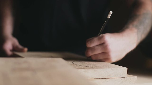 Working carpenter is drawing straight line on a piece of wood.