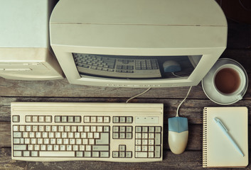 Retro stationary computer on a rustic wooden desk, vintage workspace. Monitor, keyboard, computer mouse, top view, flat lay.