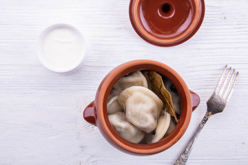 The cooked pelmeni in broth with spices and herbs with fresh sour cream