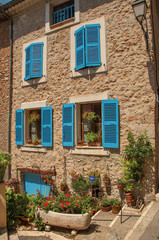Fototapeta na wymiar Facade of building with windows and blue shutters in Chateaudouble, a quiet and tourist village with medieval origin on a sunny day. Located in the Var department, Provence region, southeastern France