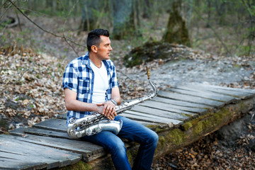 A man with the silver vintage sax outdoors on the small wooden bridge enjoying the nature
