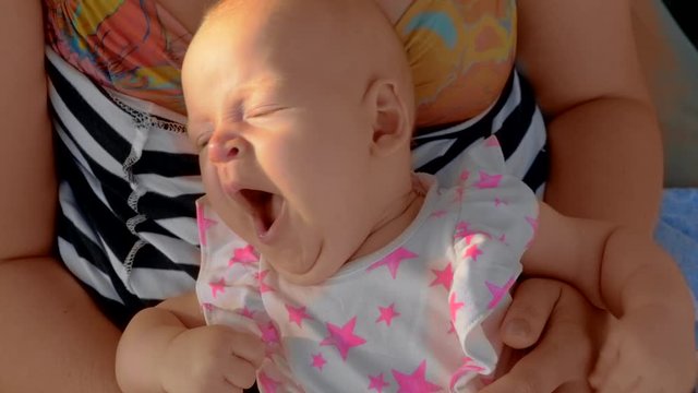 Slow motion shot of sleepy three months baby girl lying on mothers lap and yawning. Outing with mom at the beach