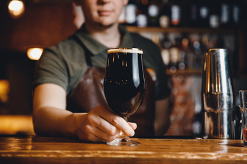 Barman serves glass of dark cold beer at bar counter.