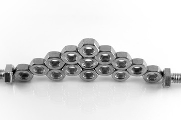 Steel hexahedral nuts stacked on top of each other in staggered order on a white background with reflection.