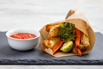 Oven baked vegetables with spices and herbs on a plate. Carrot, potato fries, brussel sprouts and broccoli with tomato sauce.