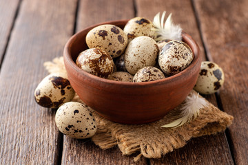 Fresh quail eggs in ceramic bowl on rustic wooden background